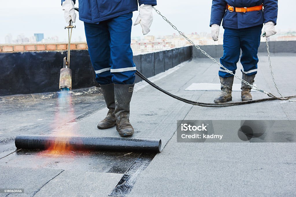 Flat roof installation. Heating and melting bitumen roofing felt Flat roof installation. Heating and melting bitumen roofing felt by flame torch at construction site Rooftop Stock Photo