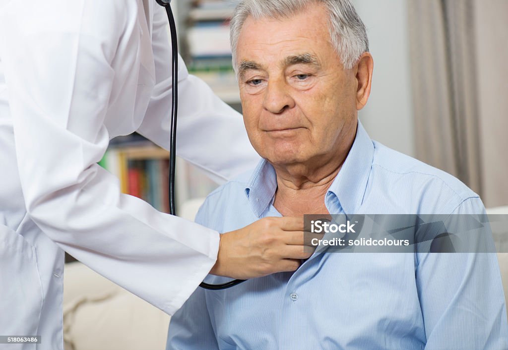 Medical Caring For Senior Man At Home Female nurse examining senior man with stethoscope at home. Doctor Stock Photo