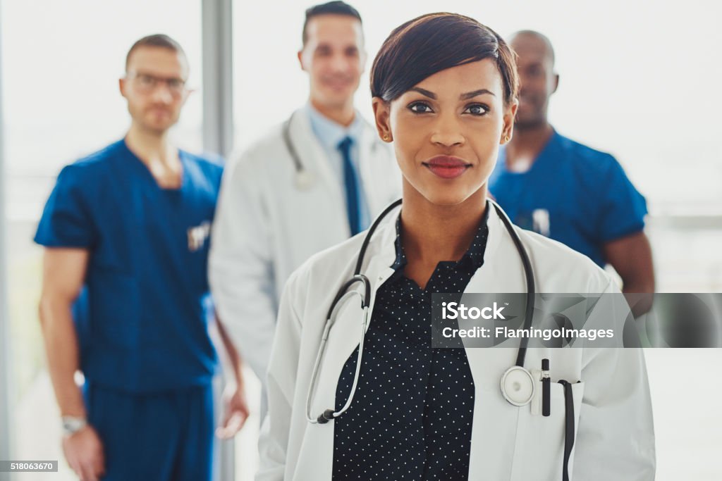 Confident female doctor in front of team Confident female doctor in front of team, looking at camera smiling, multiracial team with black female doctor Doctor Stock Photo