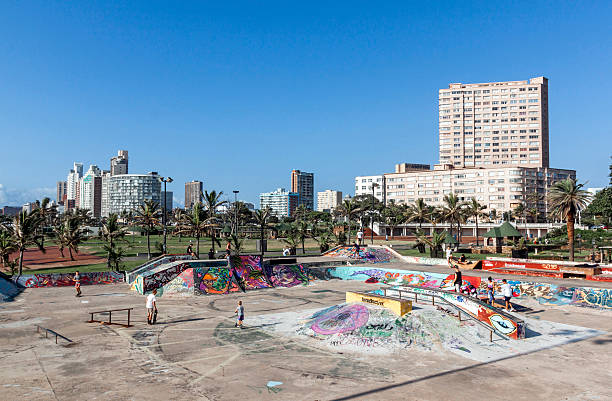 Durban, South Africa - March 23, 2016:  Many unknown childred skate boarding at colorful skate board park against city skyline on beachfront in Durban South Africa
