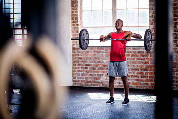 Young adult afro-american athletic man lifting barbell weights during a fitness workout at the gym