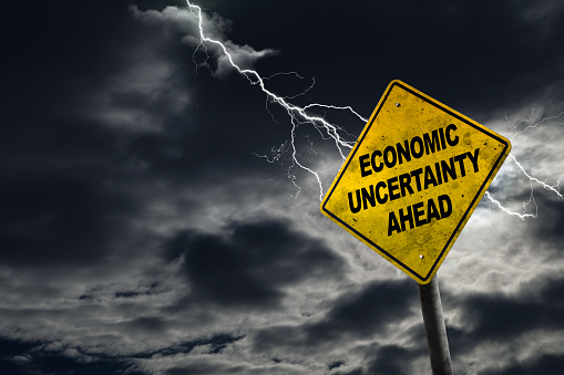 Economic Uncertainty sign against a stormy background with lightning and copy space. Dirty and angled sign adds to the drama.