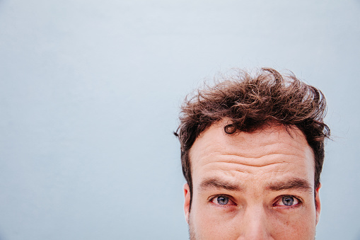 Half of the man's face with curly hair, isolated on blue wall background