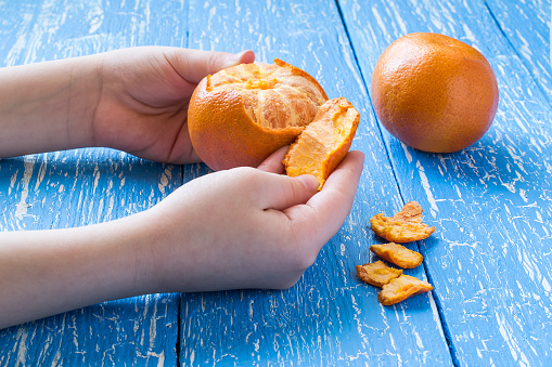 Children's hands peeling tangerine on a blue wooden table