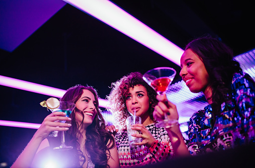 Multi-ethnic group of young adult girls drinking colorful cocktails in a night club