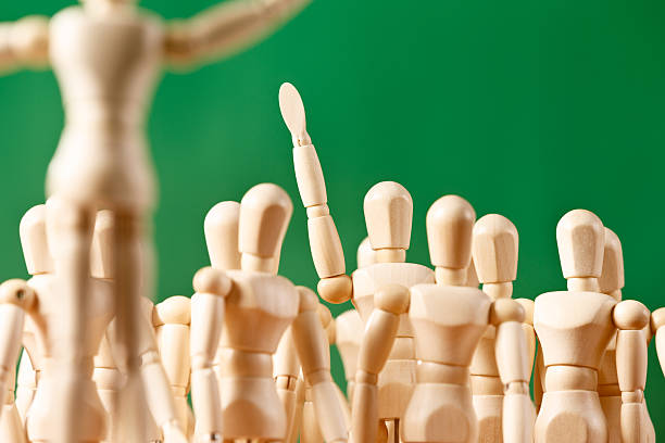 istock Single figure in crowd raises hand, querying, responding, or volunteering 518095535
