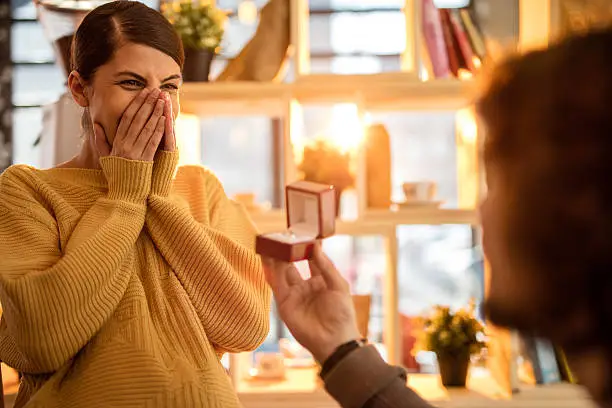 Young surprised woman being proposed by her boyfriend.