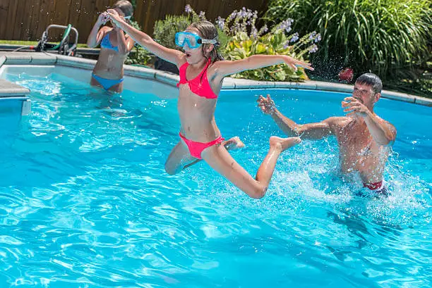 Little girl in swimwear with scuba mask in mid air above a swimming pool being thrown by her father. Her sister in the background.