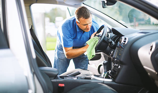 Sunday car wash. Closeup side view of mid 30's caucasian man cleaning upholstery of his car. He's sitting in driver's seat and wiping center console with soft green cloth. Both doors are ajar. This is his Sunday routine in spring and summer. Toned image. car interior stock pictures, royalty-free photos & images
