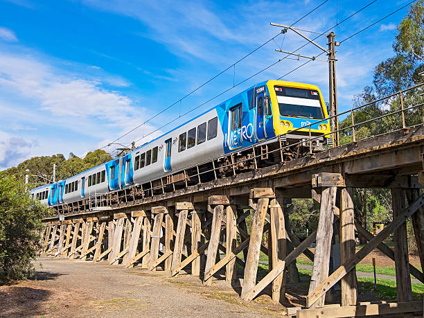 Melbourne, Australia - January 31, 2016: An UP Metro train to Flinders Street proceeds cautiously across the heritage-listed old wooden viaduct after leaving Eltham Station on Melbourne’s Hurstbridge line.  Built in 1902 for steam-era trains, the bridge over Diamond Creek is the last-remaining railway bridge built predominantly from timber still in use on the Melbourne metropolitan railway network.  While an attractive part of the river-valley environment, the old bridge is a bottleneck for modern railway operations. 