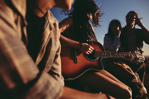 Hipster fashion group of friends is having fun together singing and playing a guitar outdoors during sunset