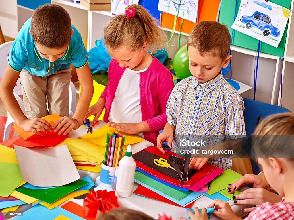 Kids holding colored paper on table in kindergarten Group kids holding colored paper on table in preschooler. Schoolyard Stock Photo