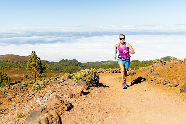 Young woman cross country running in mountains on sunny summer day. Beauty female runner jogging and exercising outdoors in nature, rocky trail footpath on La Palma, Canary Islands
