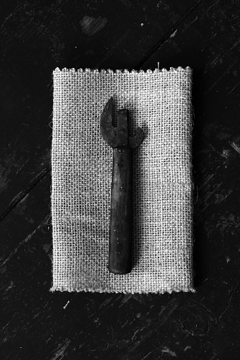 Old dirty can opener on the matting, on black boards. Top view closeup. Rustic styleThe concept of rustic kitchen. Black and white photo