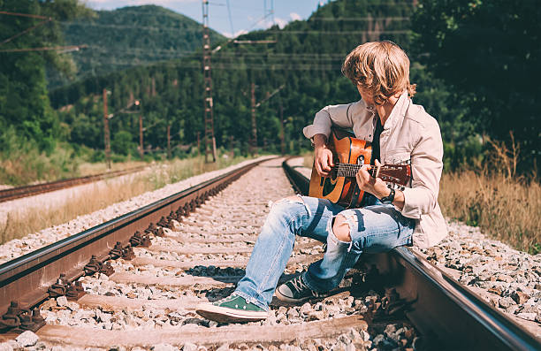 istock Young man with guitar sitting on the railway 518151530