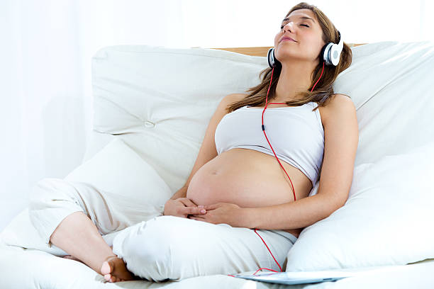 mulher grávida sentada no sofá e ouvir música em auscultadores. - babies and children audio imagens e fotografias de stock