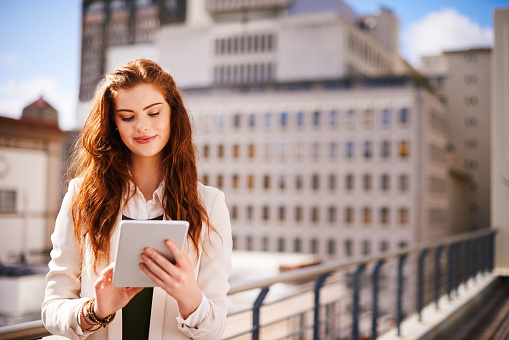 Shot of a young businesswoman using her tablet while standing on a balcony