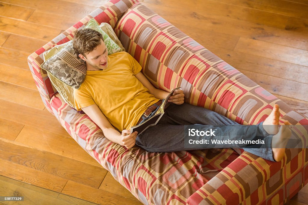 Young man reading magazine on his couch Young man reading magazine on his couch at home in the living room 20-29 Years Stock Photo