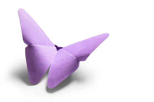 A paper origami butterfly is isolated on a plain white background. The butterfly is made from a single sheet of thin purple paper that has been precisely folded to create this shape. There is a clipping path around the butterfly and a soft drop shadow underneath it.