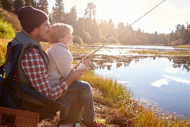 istock Father teaching son to fish sitting at lakeside 518182758