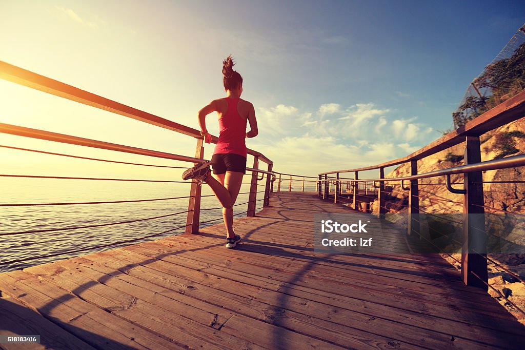 young fitness woman running on seaside wooden boardwalk Running Stock Photo