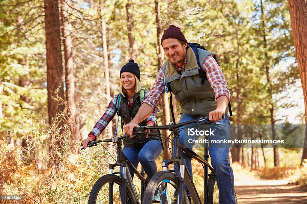 Couple mountain biking through forest, looking to camera Autumn Stock Photo