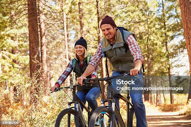 Couple Mountain Biking Through Forest Looking To Camera Stock Photo - Download Image Now