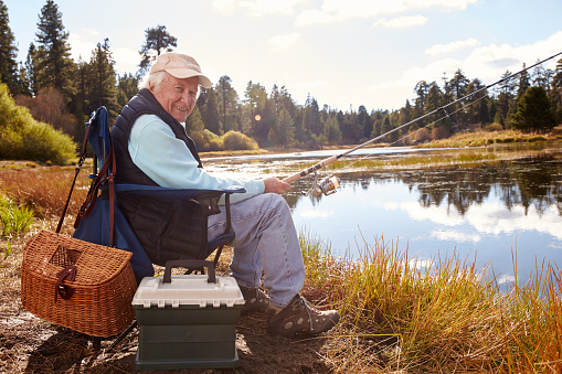 Senior man fishing in a lake, looking to camera, California