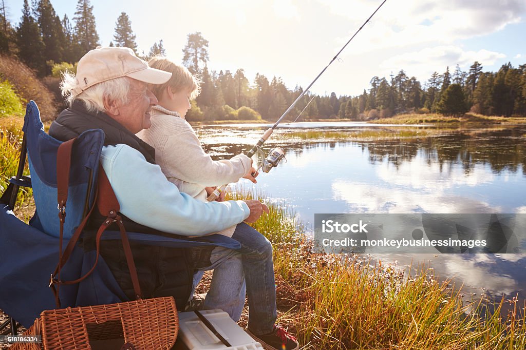 Senior man teaching his grandson to fish at a lake Fishing Stock Photo