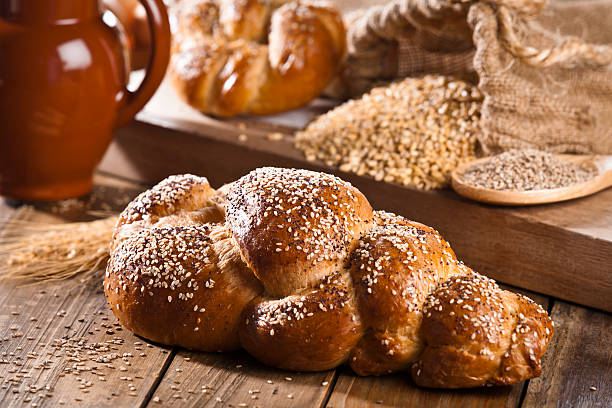 Healthy loaf of bread with sesame and poppy seeds on rustic wood table. In the background are visible some ingredients for preparing bread. Predominant color: brown. DSRL studio photo taken with Canon EOS 5D Mk II and Canon EF 70-200mm f/2.8L IS II USM Telephoto Zoom Lens