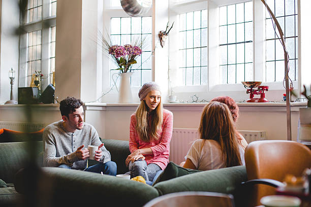 A group of friends sitting together in a coffee shop on large sofas. Drinking and talking they look relaxed and happy.