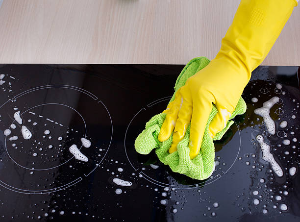 Induction hob cleaning Close up of human hand with protective gloves cleaning induction hob with green mop electromagnetic induction stock pictures, royalty-free photos & images