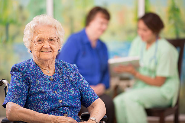 Elderly woman patient foreground. Nurse, daughter. Nursing home. Over 100 year old woman in foreground as her daughter and home healthcare nurse talk about her treatment options in background. Nursing home, doctor's office, or home setting.  over 100 photos stock pictures, royalty-free photos & images