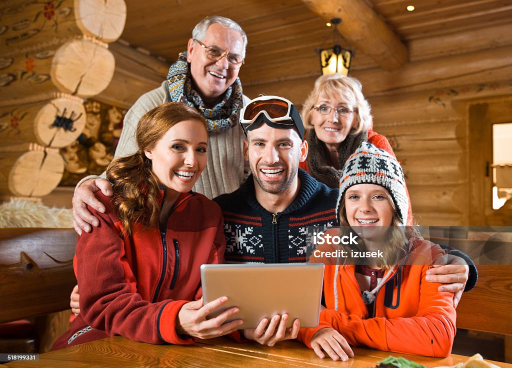 Family using digital tablet Multi-generation family sitting in a mountain restaurant after skiing and using a digital tablet together, smiling at the camera. Active Seniors Stock Photo