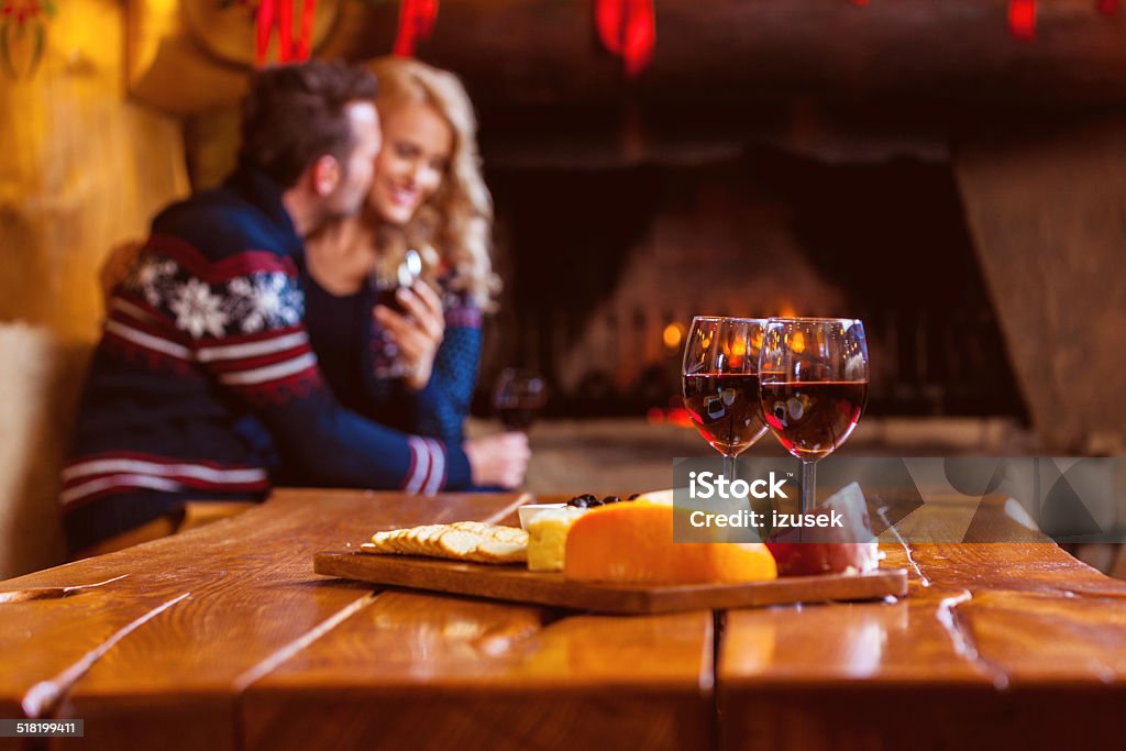 Wine and cheese Focus on four red wine glasses and chesse platter with couple flirting by fireplace in the background. Cheese Stock Photo