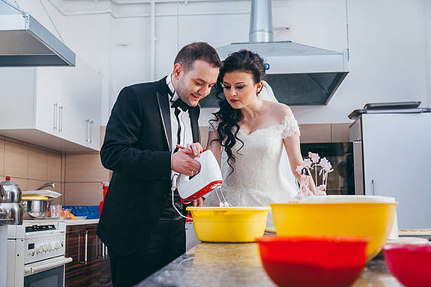 Newlywed couple mixing dough, whisking cream and preparing her wedding cake in kitchen