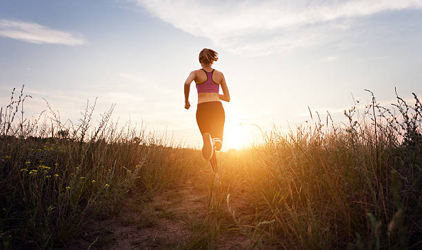 giovane ragazza sportiva corre su una strada di campagna al tramonto - hill grass park sky foto e immagini stock