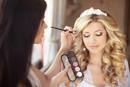 Beautiful bride wedding with makeup and curly hairstyle. Stylist makes make-up bride on wedding day. Beauty portrait of young woman at morning.