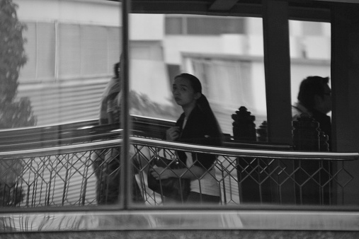 Bangkok, Thailand - January 10, 2014: People walking on Sukhumvit elevated passage way under Bts Skytrain track, reflection to a building glass facade