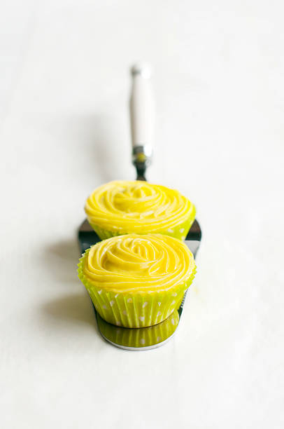 Yellow cupcakes in light green paper liners on cake shovel, white background. Selective focus