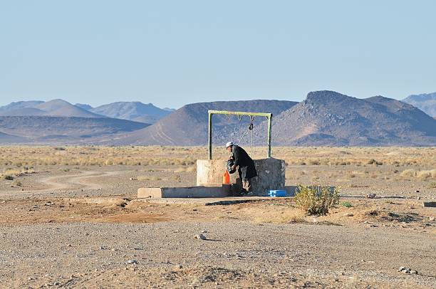 Tsar Touroug, Morocco - February 23, 2016: A Berber Moroccan man fills water containers at a well in the remote desert between El Jory and Tsar Touroug, Morocco in the morning. His truck has overheated and is sitting on the roadside making steam, He is fortunate to have this well available.