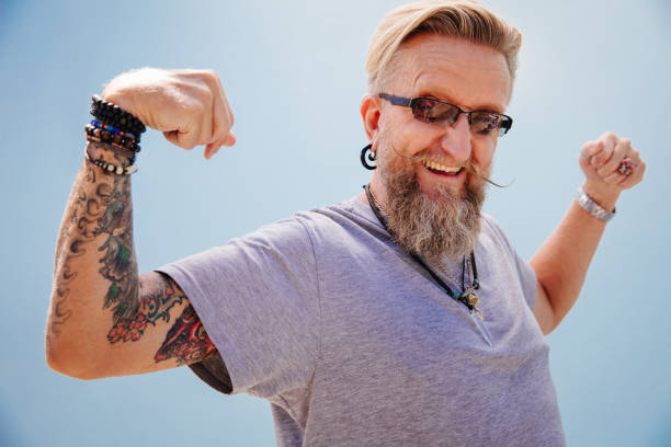 Close up of silly  mature man showing his muscles to the camera, isolated on blue wall background