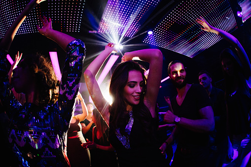 Young women dancing happily with her friends in a nigh club party with disco lights