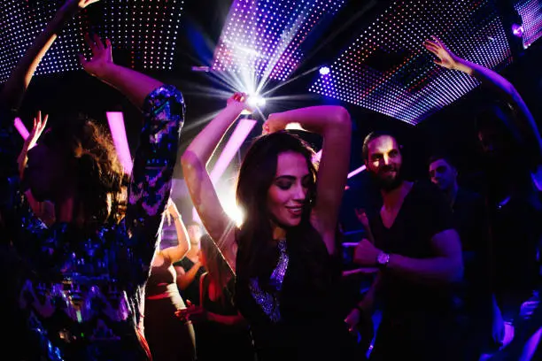 Young women dancing happily with her friends in a nigh club party with disco lights