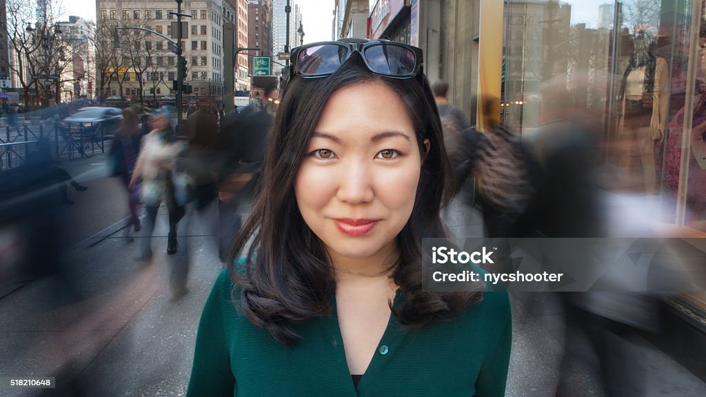 City girl portrait Beautiful young Asian woman standing on busy city sidewalk with people walking all around her. portrait close-up looking at camera. Crowd of People Stock Photo