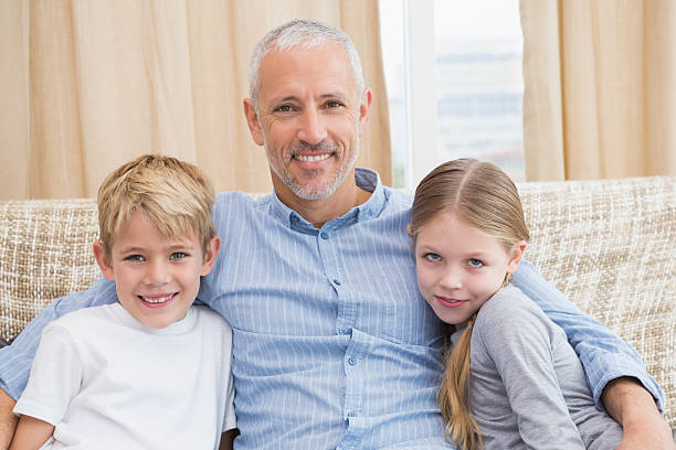 istock Father smiling at camera with his children on sofa 518220319