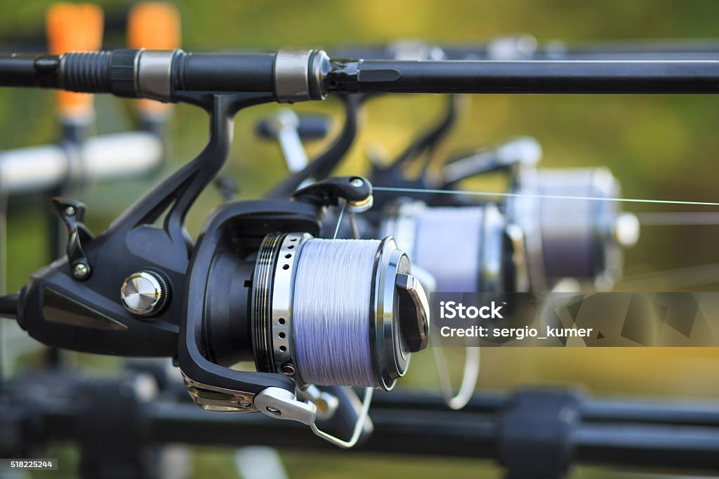 Three fishing rods with reel set up on holder Three fishing rods with professional reel set up on support. Activity Stock Photo