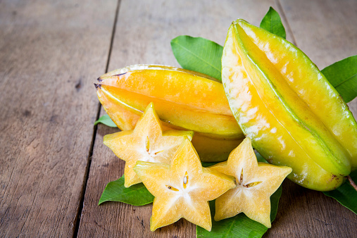 Star fruit with green leaf on wood background .