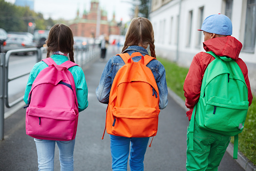 Backs of schoolkids with colorful rucksacks moving in the street