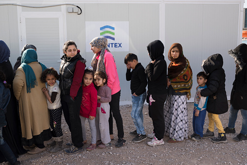 Chios, Greece - March 18, 2016: A line of women and children refugees waiting for being served breakfast by volunteers of the Norwegian NGO Drop in the Ocean just outside the Chios Port refugee camp. The refugees have arrived few days earlier by boat from the Turkish coast to the beaches of the Greek Island, Chios.